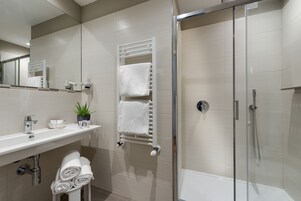 Un baño moderno con ducha envuelta en vidrio, un lavabo blanco con espejo y toallas ordenadamente dobladas.