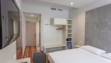 A hotel room with a bed, a TV, a desk, a chair, a wardrobe, and a shelf with clothes.