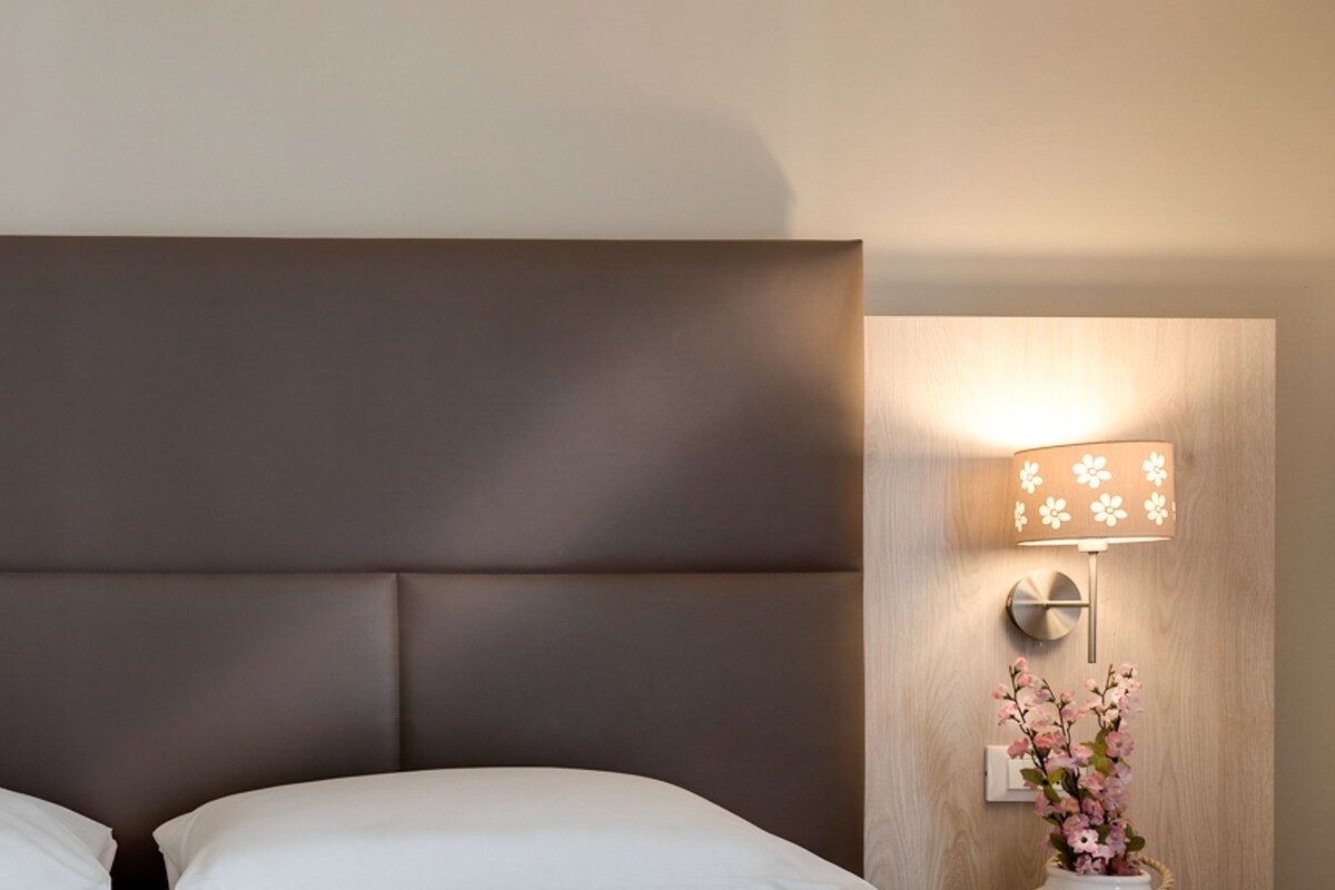 A hotel room with a large bed, two wall-mounted lamps, and a power outlet.