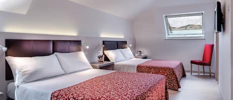 Habitación de hotel con dos camas, una silla roja, un televisor y una ventana con vistas.