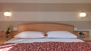 A hotel room with a wooden headboard, two white pillows, a red patterned bedspread, and two wall-mounted light fixtures.