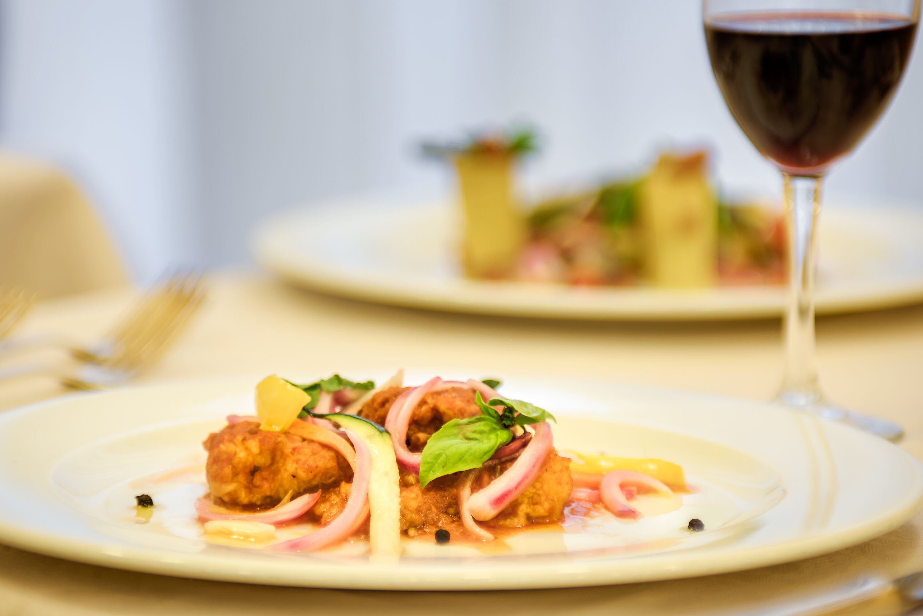 A dining table with plates of food and a glass of red wine.