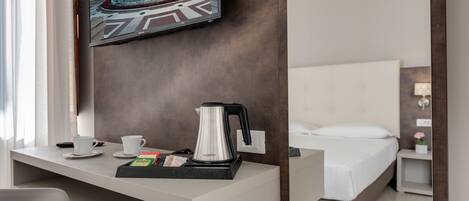 Habitación de hotel con cama, escritorio con cafetera, televisor montado en la pared y vista a la piscina.