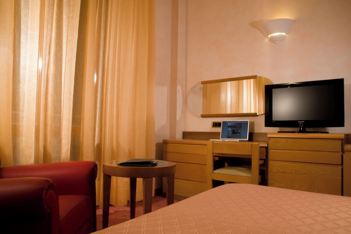 Een hotelkamer met een bed, een bureau, een stoel, een televisie en een lamp.