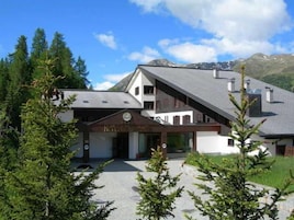 Un hotel con diseño arquitectónico moderno, que destaca por su entrada imponente y un telón de fondo montañoso.