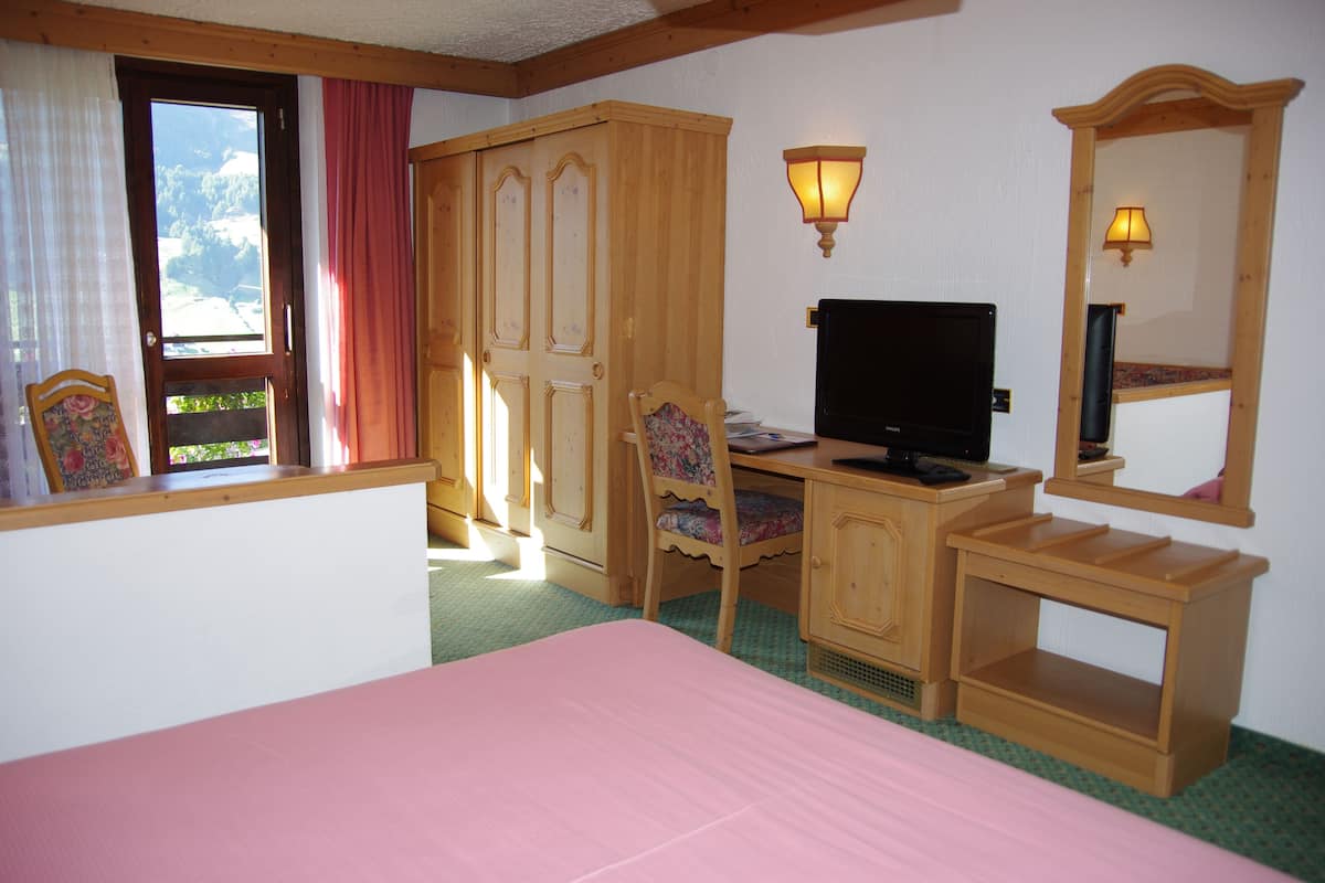 A bedroom with a bed, a desk, a chair, a television, and a wardrobe.