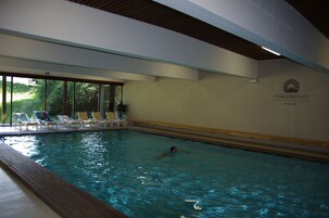 Una piscina interior con agua cristalina, sillones de descanso y vistas a zonas verdes.