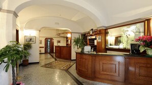 Eine Lobby mit einer gebogenen Rezeption, Blumentöpfen und einem polierten Marmorboden.