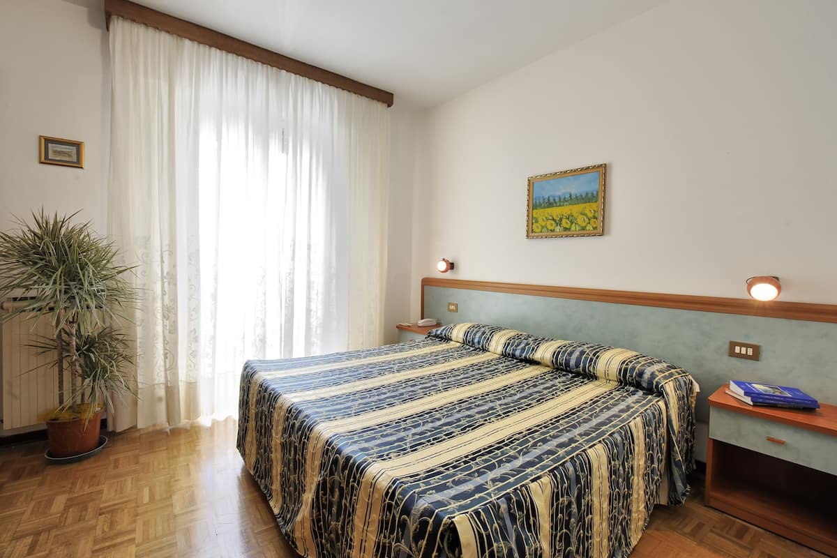 A bedroom with a bed, a nightstand, a lamp, a potted plant, and a painting on the wall.