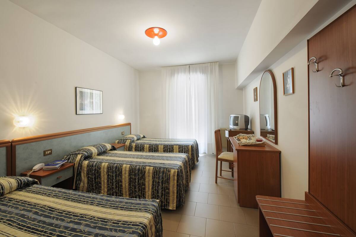 A hotel room with two beds, a desk with a chair, a television, and a wardrobe.