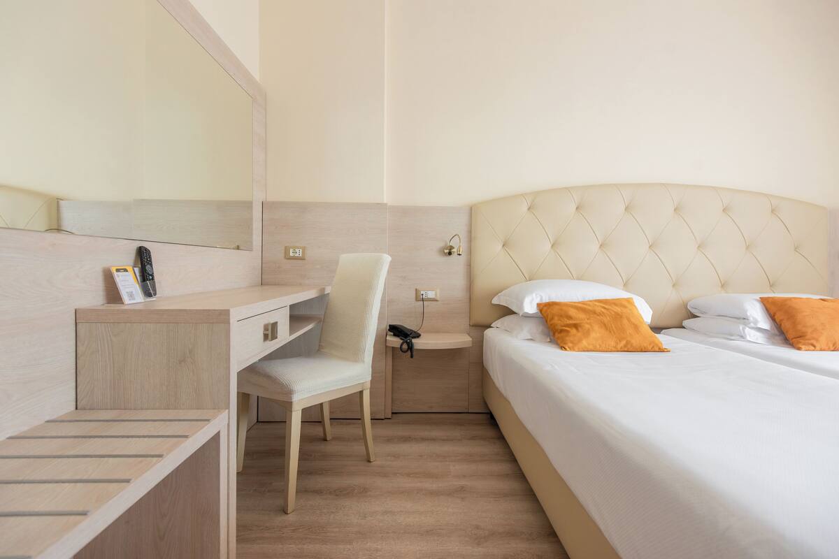 Ein Hotelzimmer mit Bett, Schreibtisch, Stuhl, Nachttisch und Spiegel.