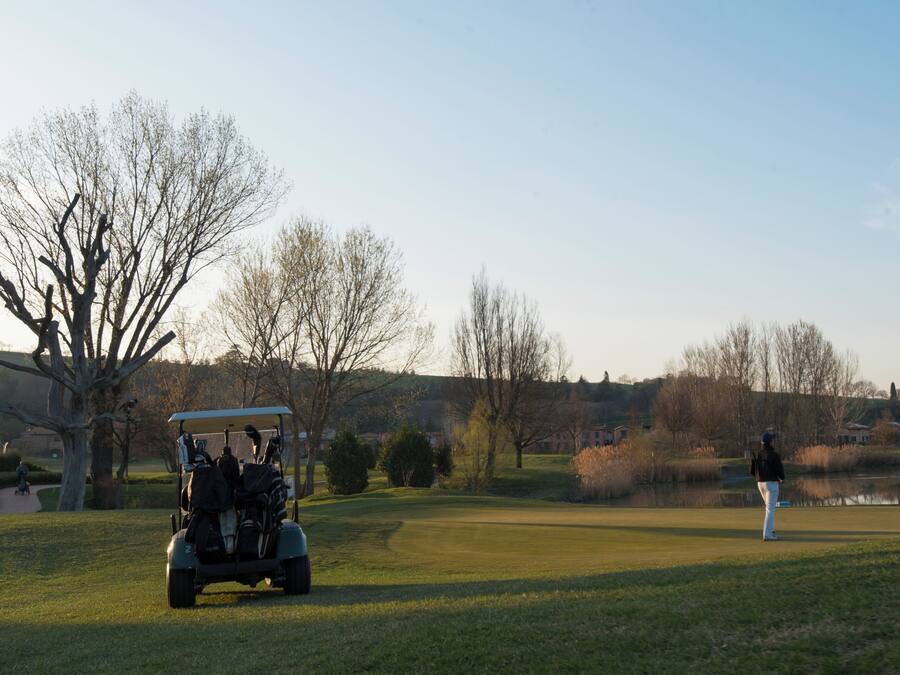 A golf course with a cart and a person standing in the distance.