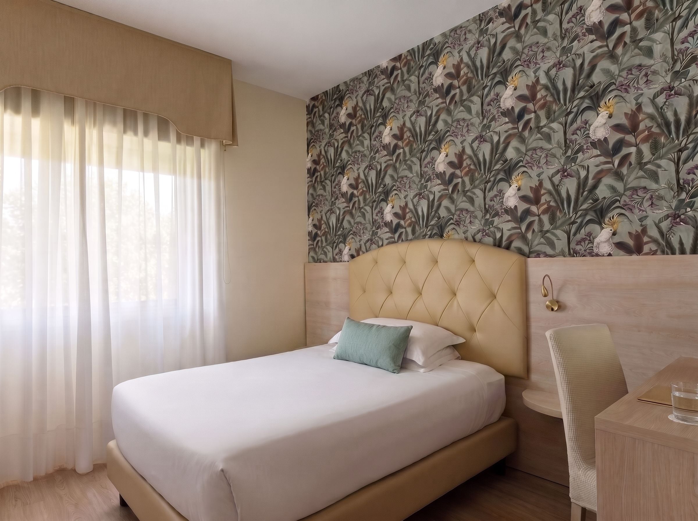 A hotel room with a bed, a chair, a desk, and a wall with a floral pattern.