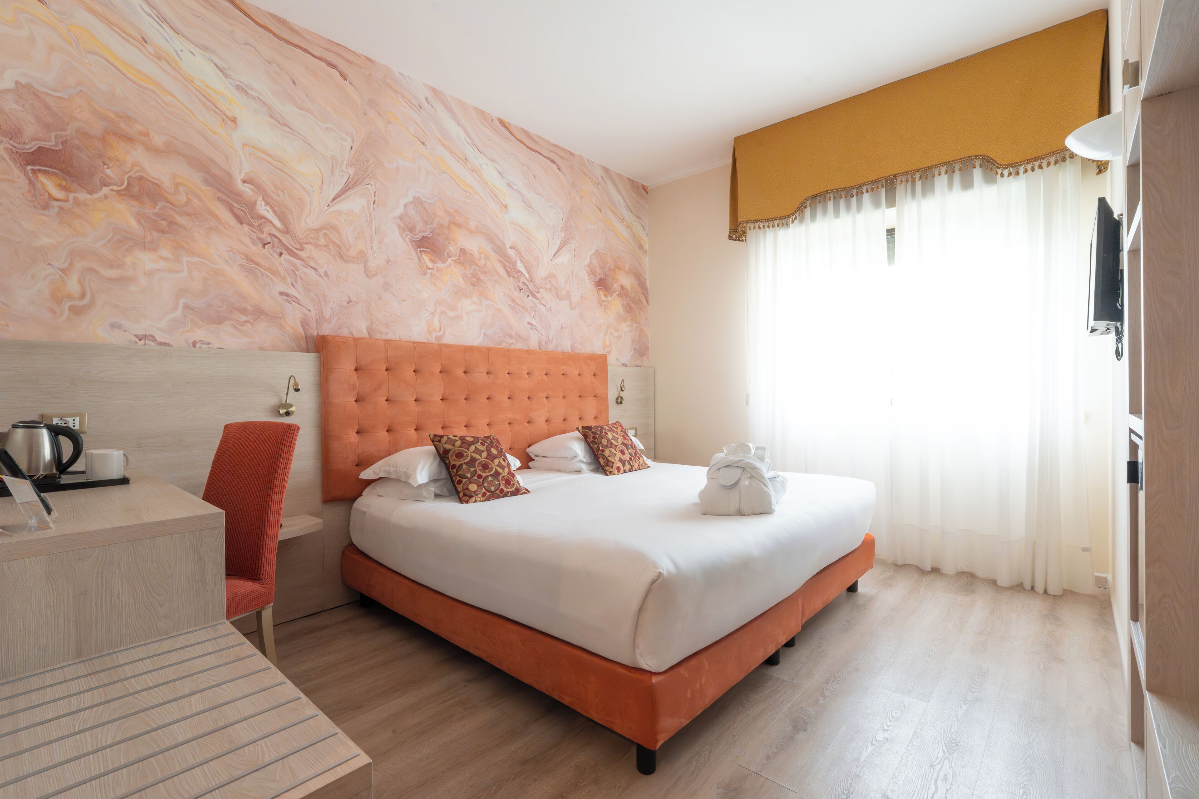 A hotel room with a large bed, a desk with a chair, a marble wall, and a window with curtains.