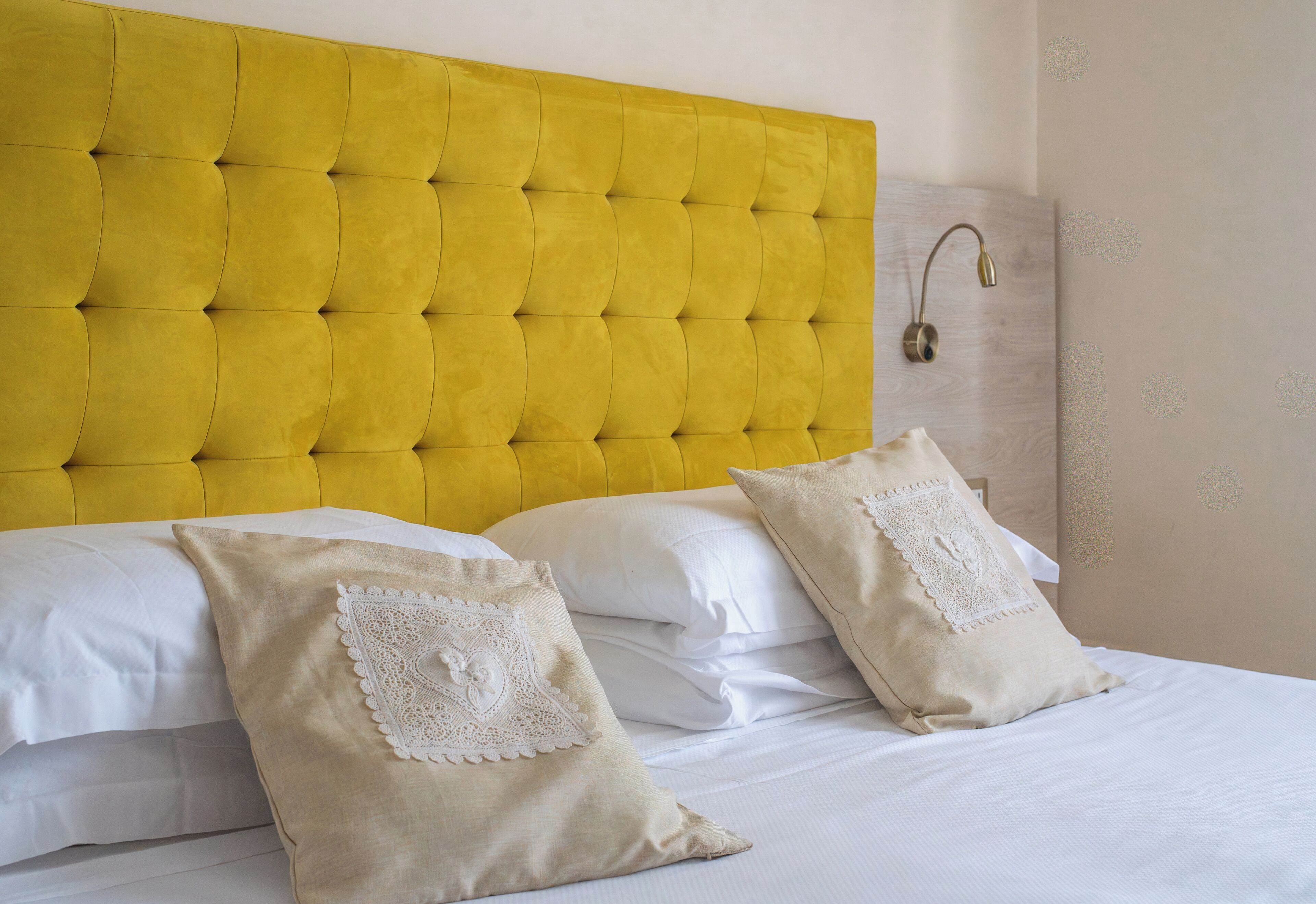 A bed with a yellow tufted headboard, white linens, and two decorative pillows.