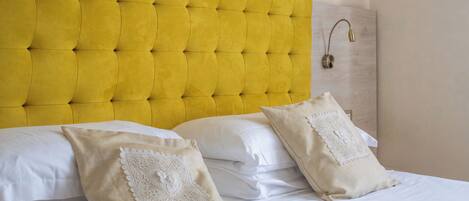 Un lit avec une tête de lit jaune à motifs capitonnés, du linge de lit blanc et deux coussins décoratifs.