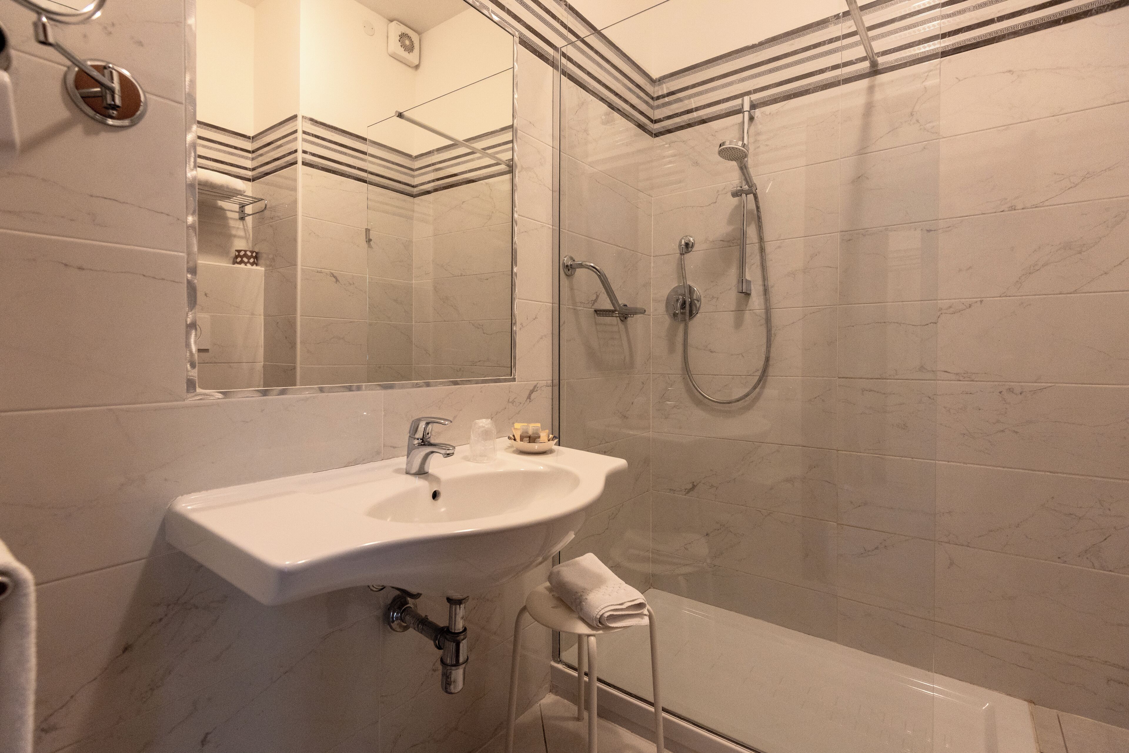Een moderne badkamer met een wit wastafelblad, een douchecabine met glazen wanden en een betegelde muur van marmer.