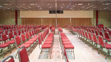 A large hall with rows of red chairs and a stage at the front.