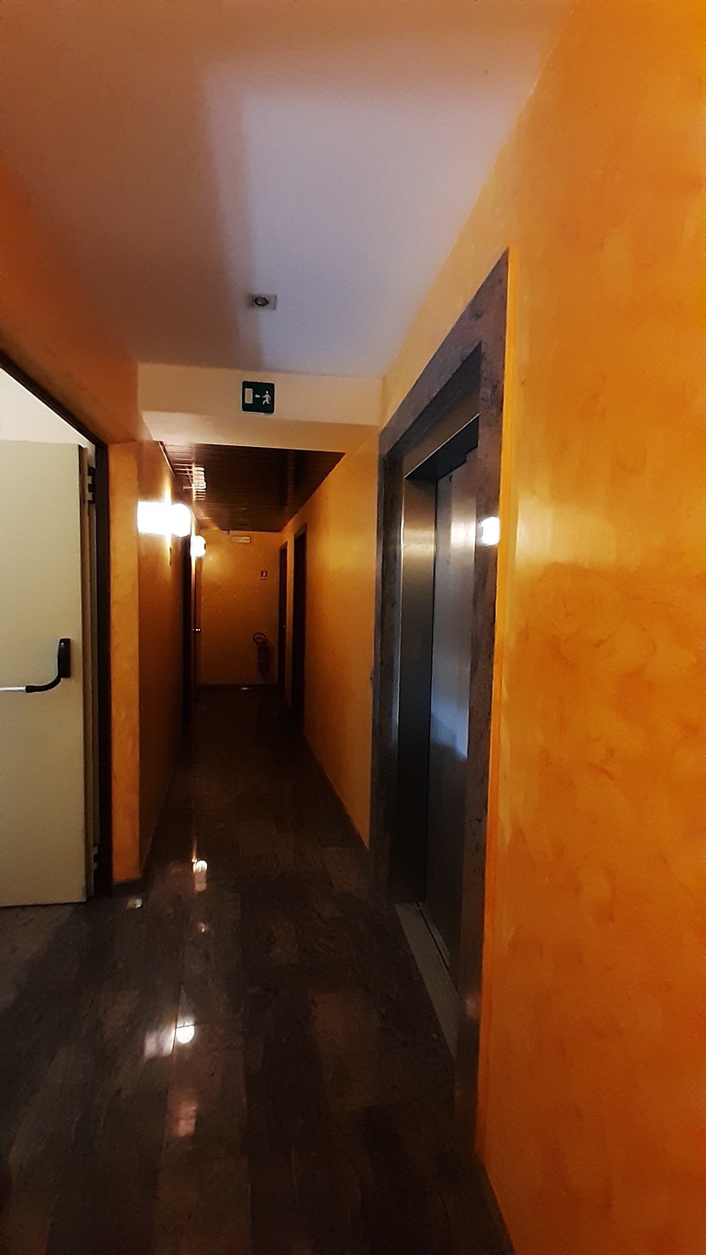 A hotel corridor with a shiny floor, a door on the left, and an elevator on the right.