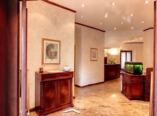A hallway with a wooden cabinet, framed artwork, and a fish tank. - Hotel Valentino (Orvieto)