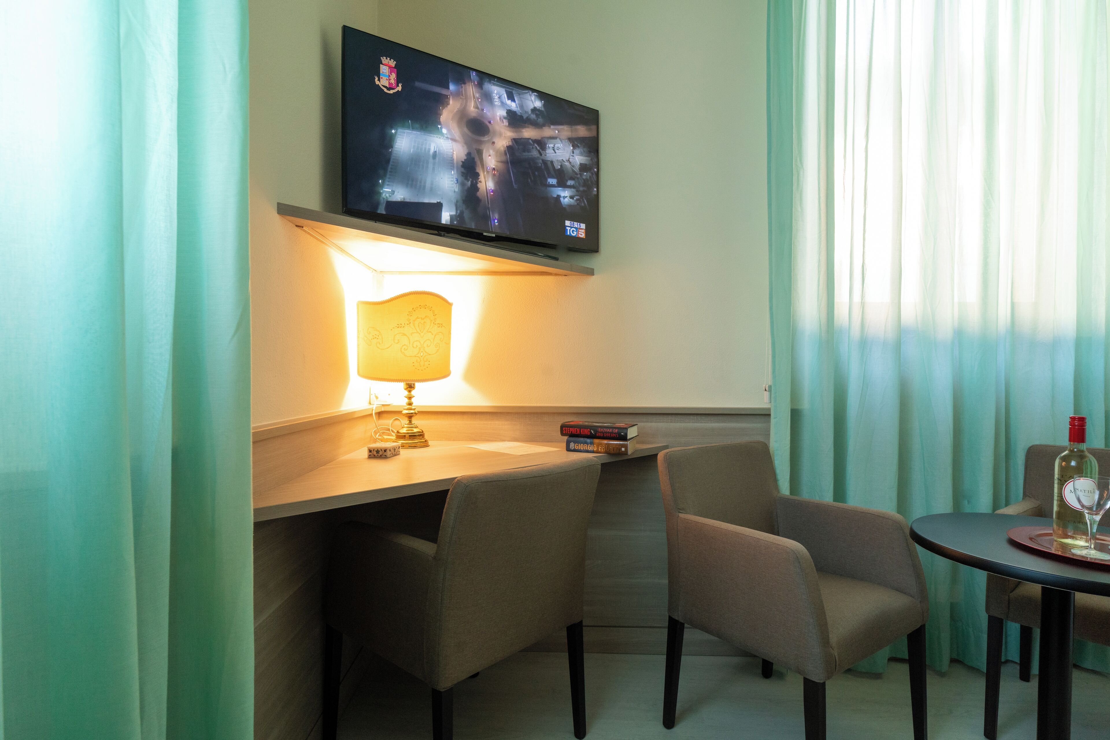 Habitació d'hotel amb escriptori, dues cadires, televisió penjada a la paret, làmpada i taula amb ampolla i vas.