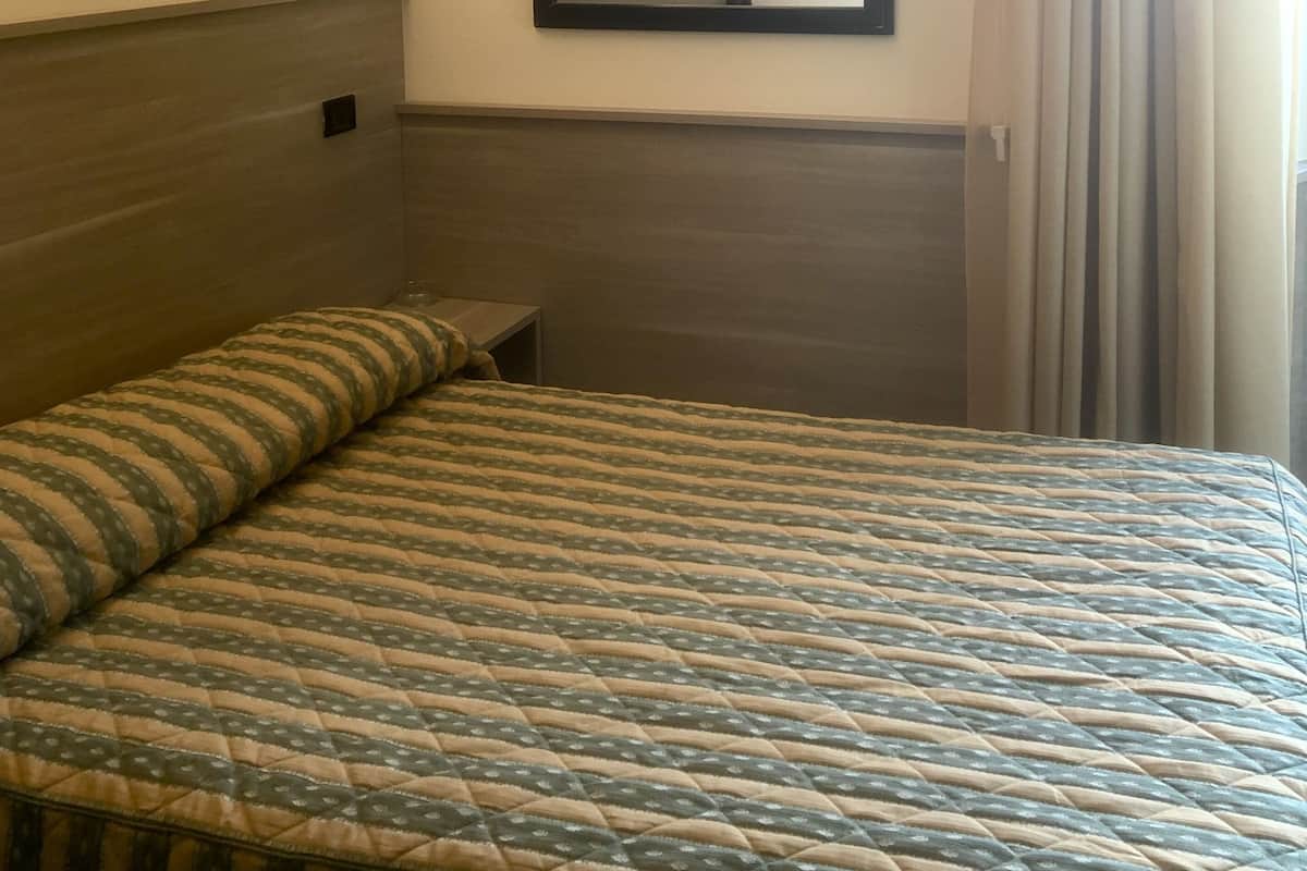 A hotel room with a bed, a bedside table, a mirror, and a painting on the wall.