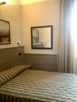 A hotel room with a bed, a bedside table, a mirror, and a painting on the wall.