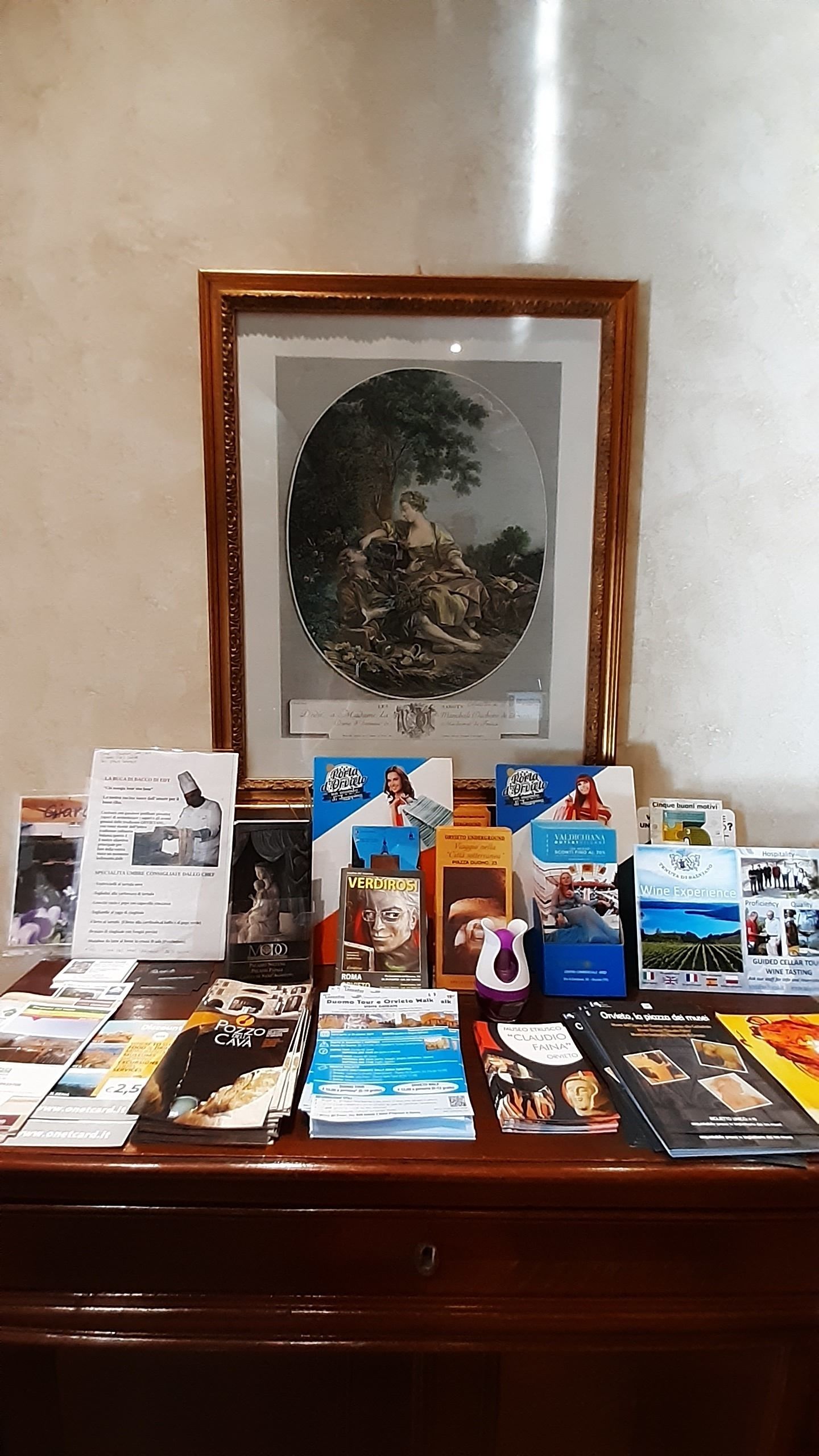 Un bureau avec des brochures, un tableau encadré et un verre à vin.