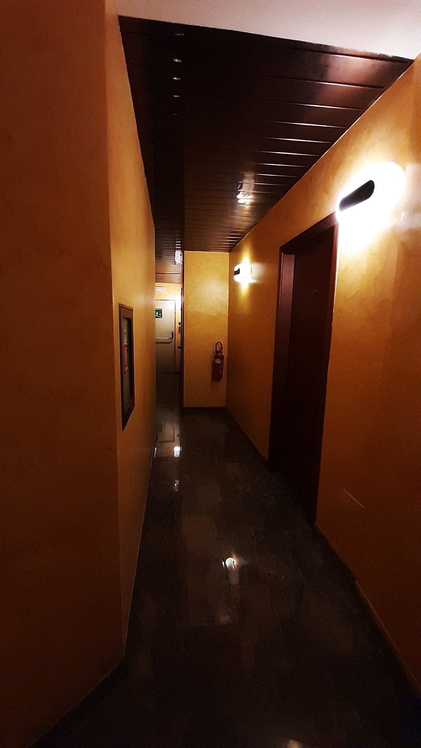 Un pasillo con piso pulido, paredes de tono cálido e iluminación empotrada en el techo.