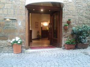The entrance of Hotel Valentino with a stone facade, a wooden door, and potted plants. - Hotel Valentino (Orvieto)