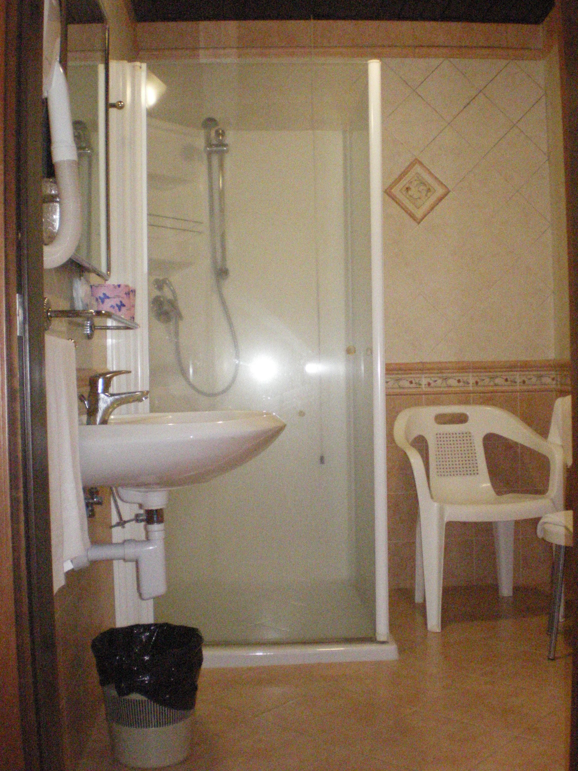 Un baño con ducha de vidrio, un lavabo y una silla de plástico blanco.