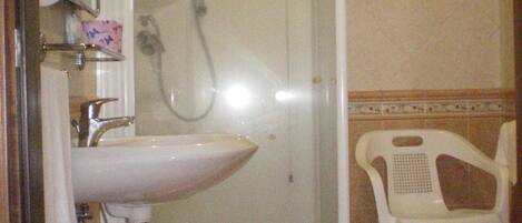 Un baño con ducha de vidrio, un lavabo y una silla de plástico blanco.