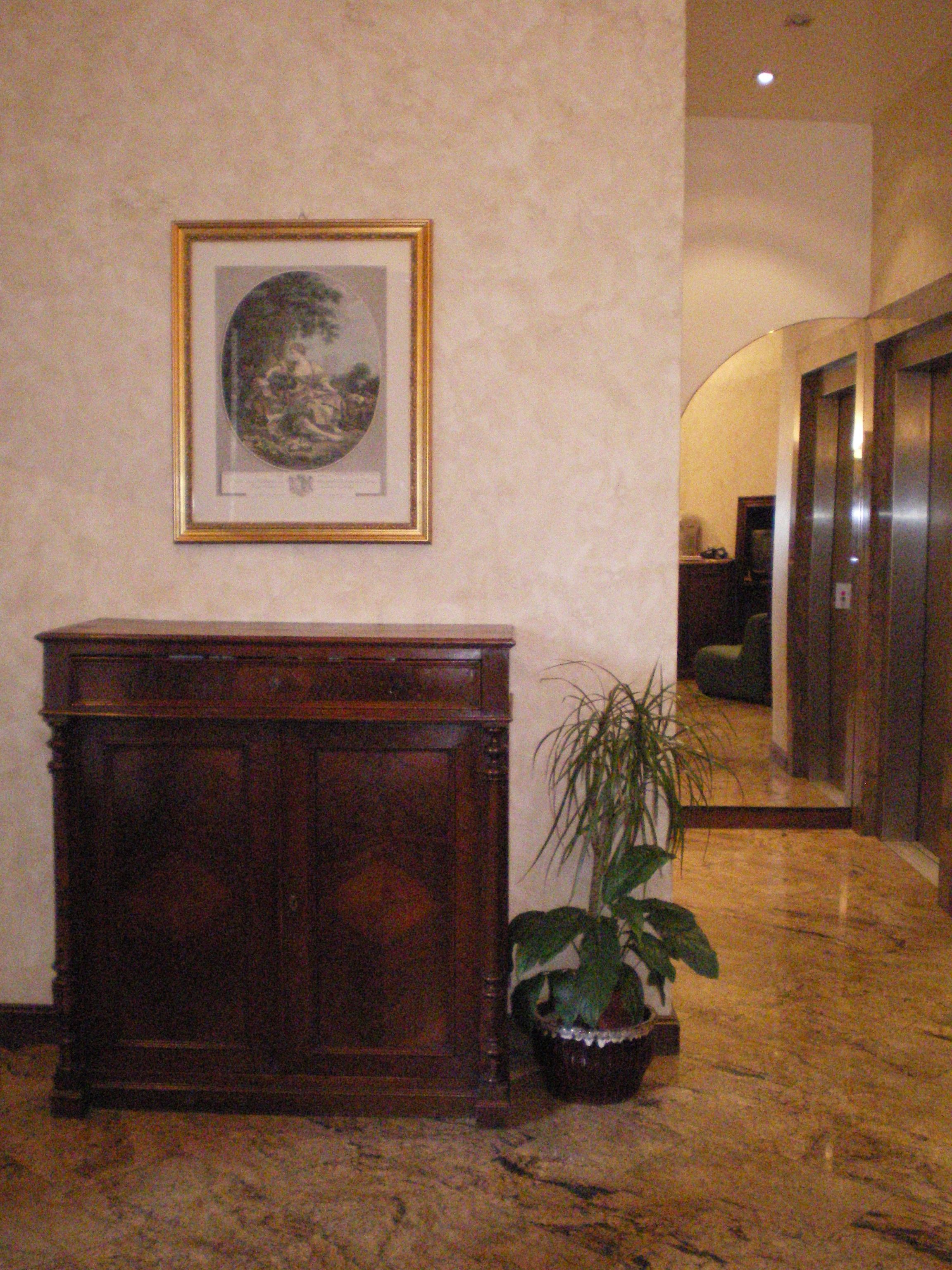 A lobby with a wooden reception desk, a framed artwork on the wall, and a potted plant.