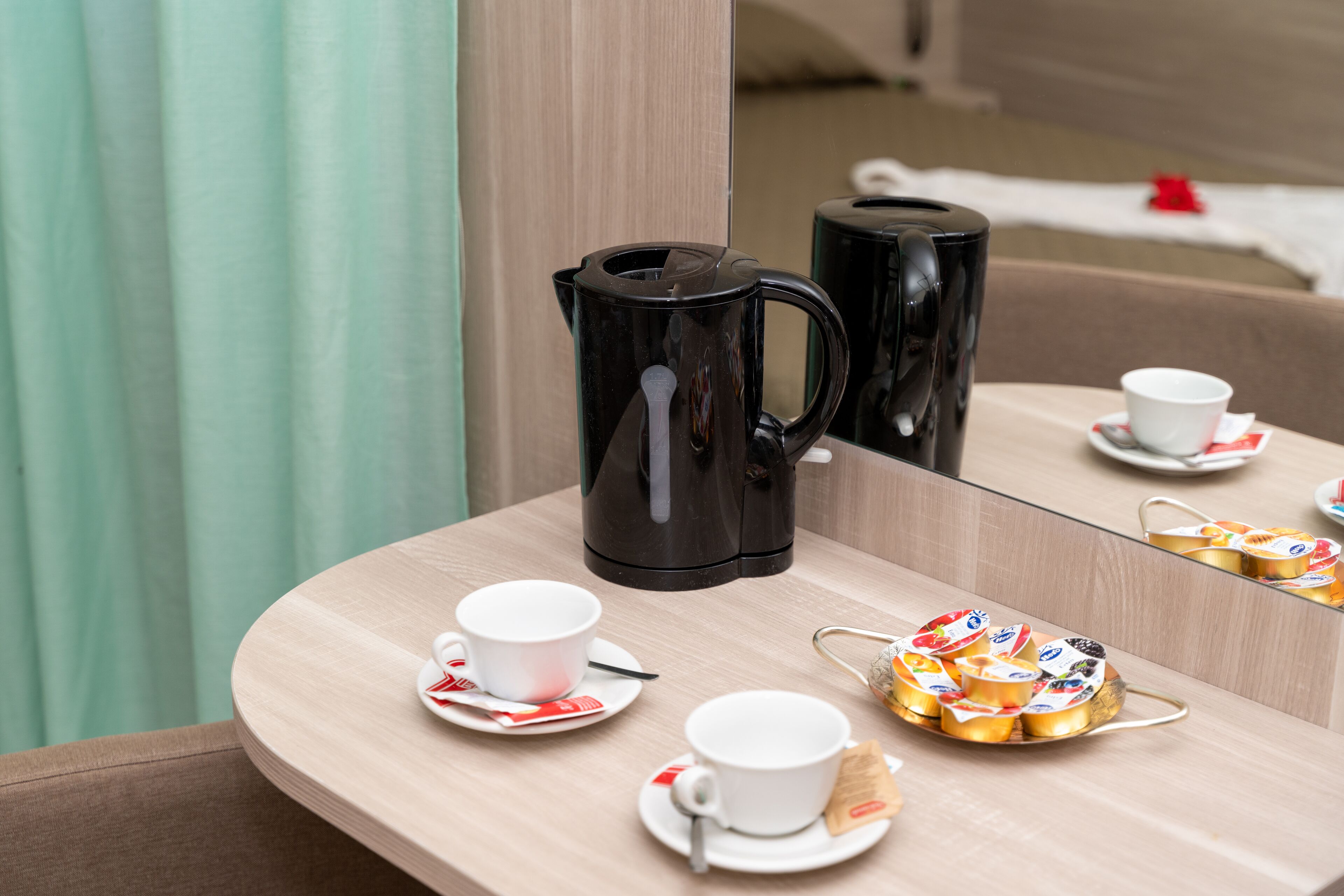 Una mesa de desayuno ordenada con una cafetera, tazas, platillos y una bandeja de pasteles.