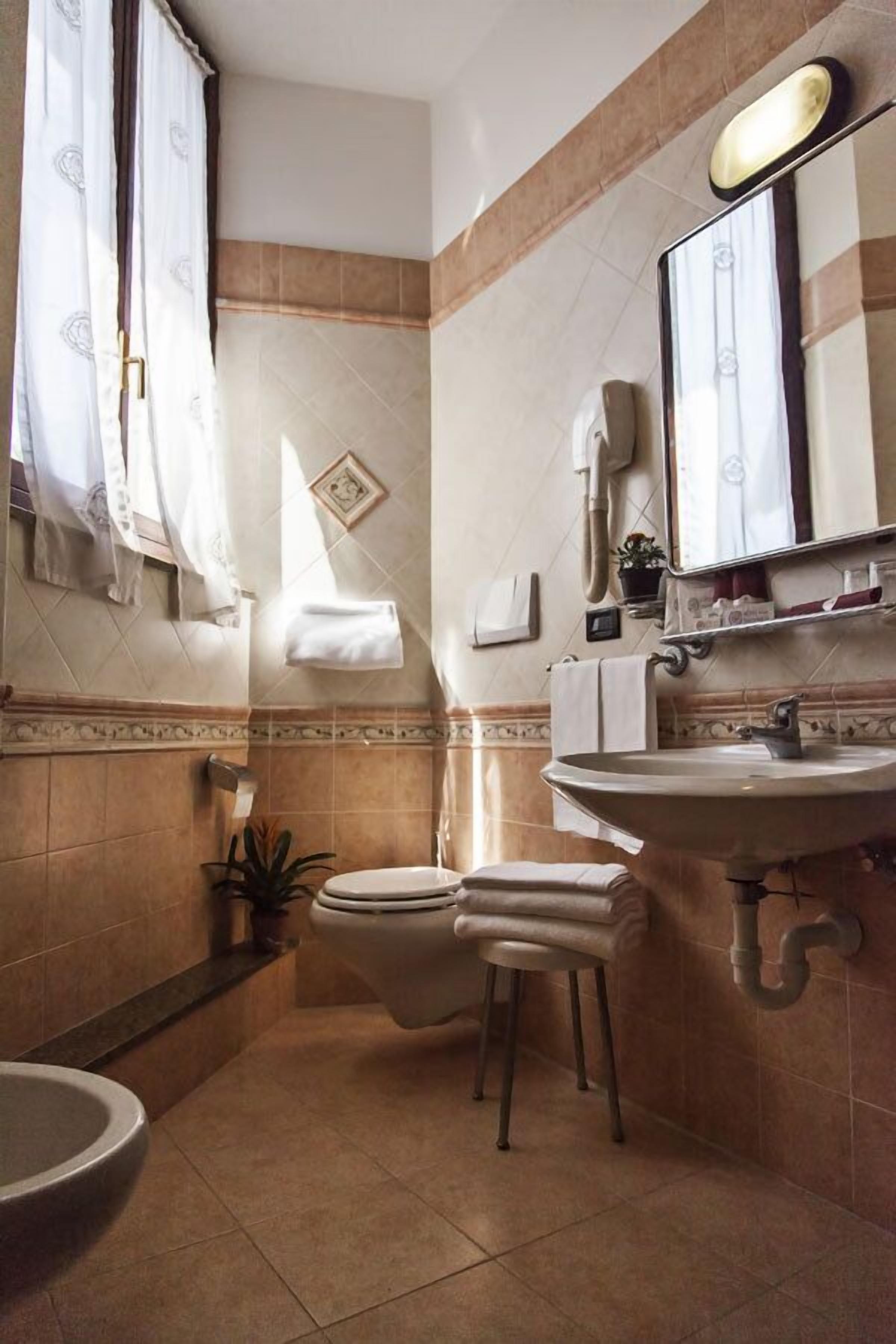 A bathroom with a toilet, sink, and mirror. There are towels and a plant on the counter.