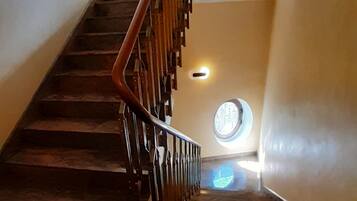 Una escalera con barandilla de madera y un ventanal circular en la parte superior.