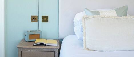 A bedroom with a white headboard, a bedside lamp, a radio, and a book on a wooden nightstand.