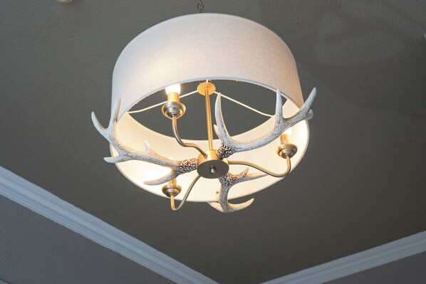 Un candelabro con pantalla blanca y brazos de metal que recuerdan a astas.