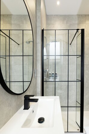 A modern bathroom with a large mirror, a white sink, and a glass-enclosed shower area. - The Royal Hotel (Bideford)