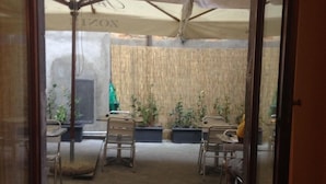 Une porte ouverte donne sur un patio aménagé avec une table et des chaises, un espace salon abrité et des plantes en pot.