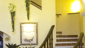 Un escalier avec une rampe en bois, un luminaire fixé au mur et deux plantes en pot.