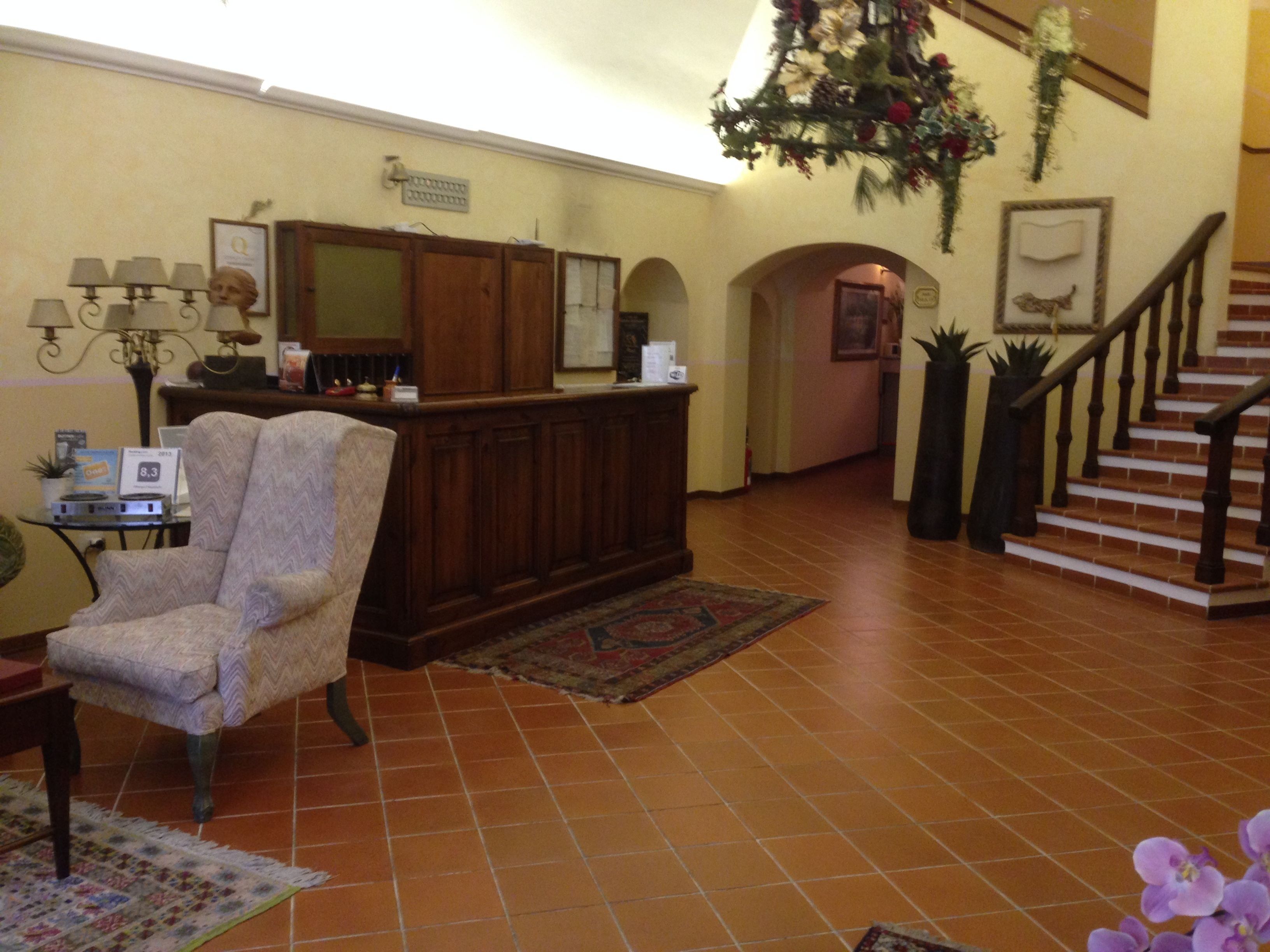 Un ampio soggiorno con un mobiletto in legno, una poltrona con motivi decorativi e una scala che conduce a un piano superiore.