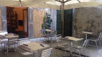 Ein Außenbereich eines Cafés mit Metalltischen und -stühlen, der von Sonnenschirmen mit dem Schriftzug 'ZONIN' beschattet wird.