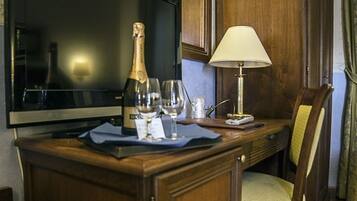 A wooden desk with a television, a bottle of champagne, two wine glasses, and a lamp.