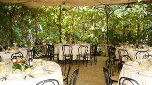 An outdoor dining area with round tables covered in white tablecloths, black metal chairs, and wine bottles. - Hotel Paradiso (Spoleto)