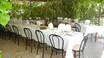An outdoor dining area with tables covered in white tablecloths and black chairs.