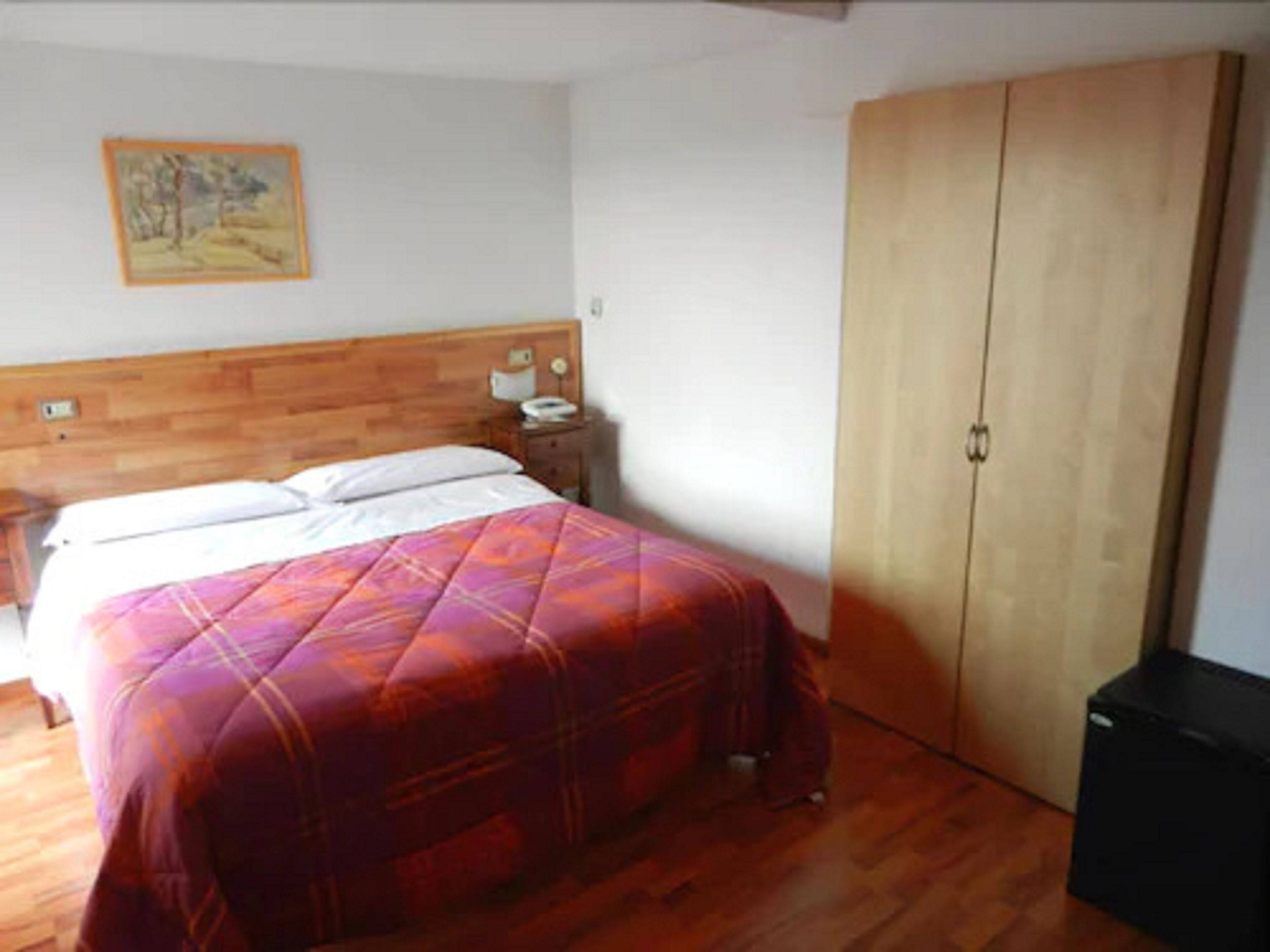 A bedroom with a wooden headboard, a bed with a colorful quilt, a nightstand with a lamp, and a wardrobe.