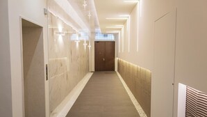 Un pasillo moderno con un muro de mármol, un revestimiento estampado a la derecha y una puerta de madera al final.