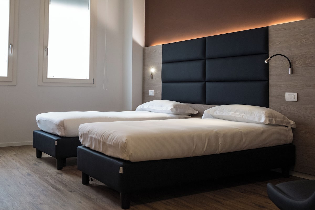 A bedroom with two beds, a wooden headboard, and a wall-mounted light fixture.