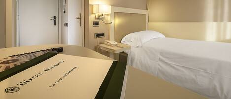 A hotel room with a bed, a bedside table with a lamp, a phone, and a door.